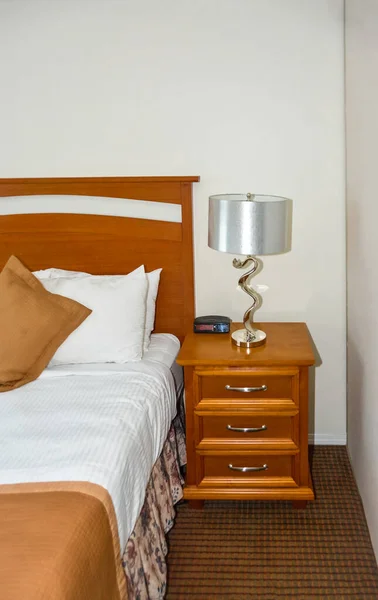 Silver lamp and radio watch on wooden bedside table beside the bed