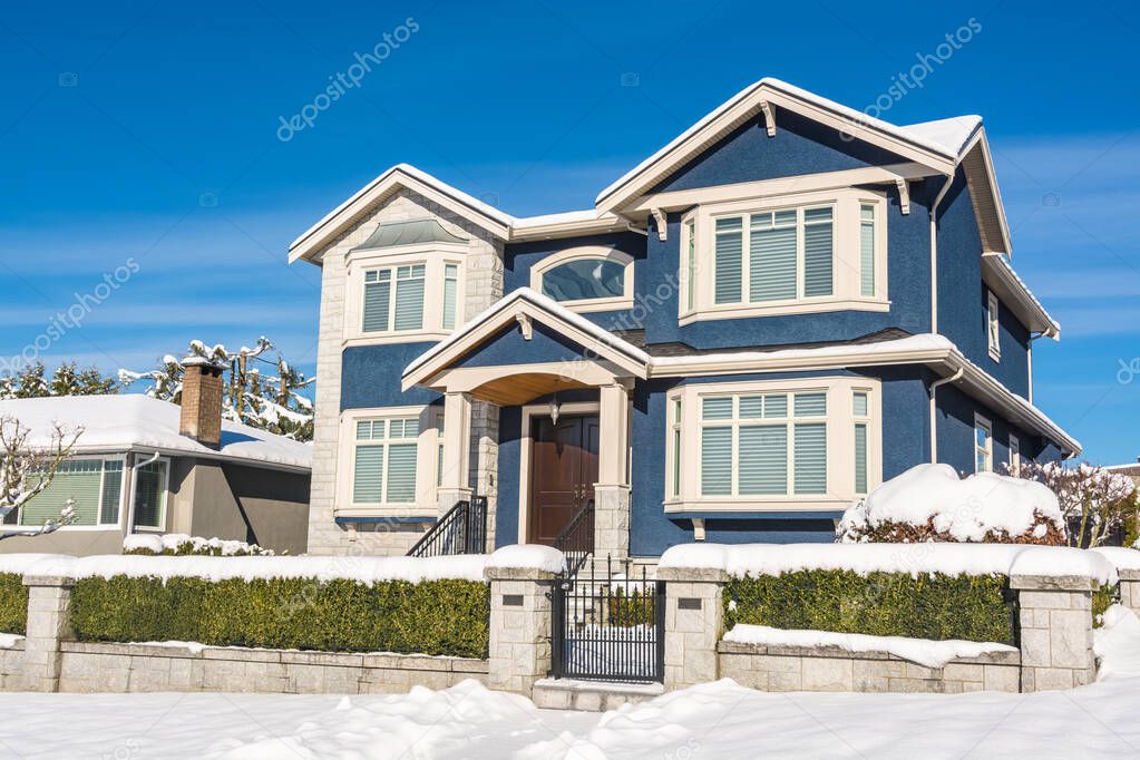 Luxury residential house with front yard in snow on winter sunny day