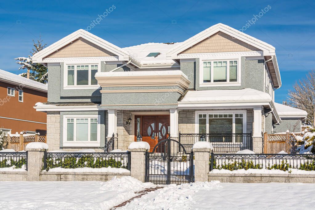 Luxury residential house with front yard in snow on winter sunny day