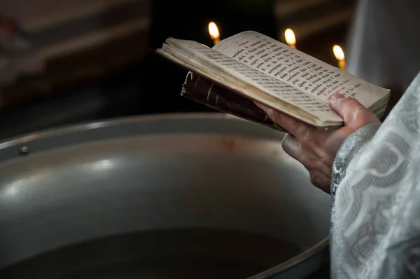 Священник молится в церкви, держа в руках святую Библию и крест со свечами — стоковое фото