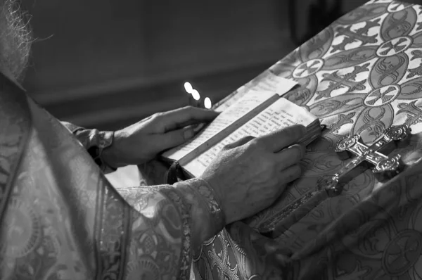 Prêtre noir et blanc priant dans l'église tenant la bible de houx et croix avec des bougies — Photo