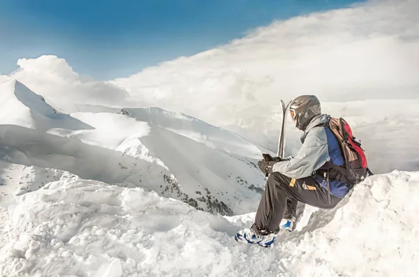 Snowboarder assis avec snowboard dans les mains est assis sur un gros rocher sur fond de montagnes. Bansko, Bulgarie — Photo