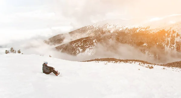 Panorama avec snowboarder assis avec snowboard dans les mains assis sur bi — Photo