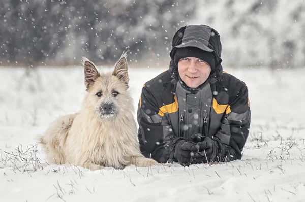 Człowiek i pies są szczęśliwi leżąc w zimie śniegu — Zdjęcie stockowe
