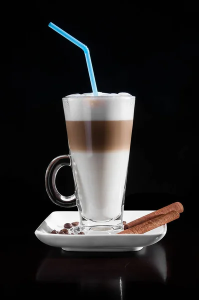 Latte macchiato beyaz tabak, kaşık, kahve çekirdekleri, tarçın ile süslenmiş bir bardak. Siyah arka plan.