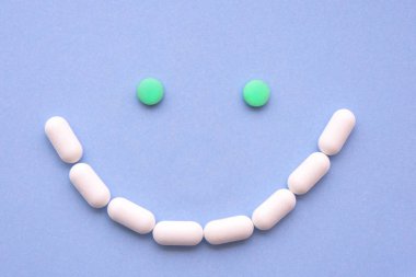 Mavi arka plan üzerinde büyük bir gülen gibi birkaç farklı hap türleri ve renkleri