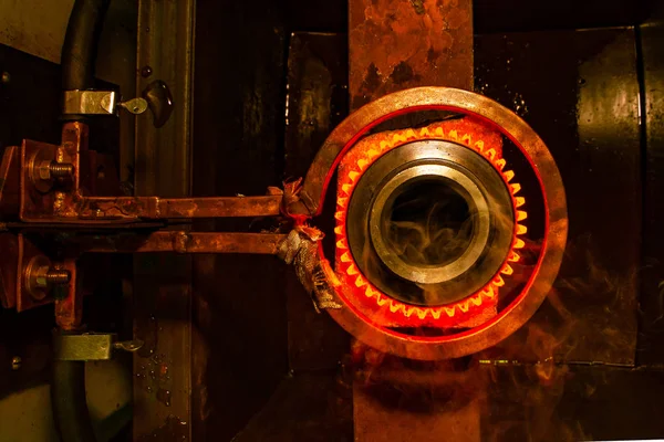 closeup calcining hot metal steel gear parts in a factory induction furnace with smoke