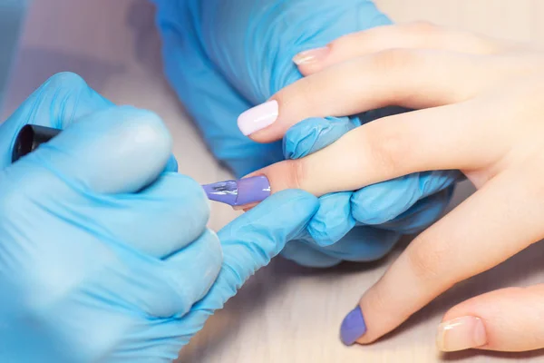 Closeup healthy natural woman\'s nails in beauty salon. Manicurist hand painting client\'s nails. Covering nails with gel-lacquer.