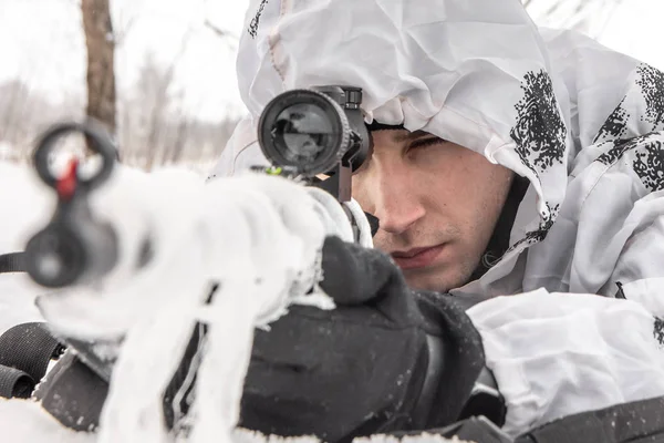 Retrato de cerca Hombre soldado en el invierno en una cacería con un rifle de francotirador en camuflaje blanco de invierno que yace en la nieve — Foto de Stock