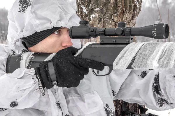 Retrato de cerca Hombre soldado en el invierno en una cacería con un rifle de francotirador en camuflaje blanco de invierno que yace en la nieve — Foto de Stock