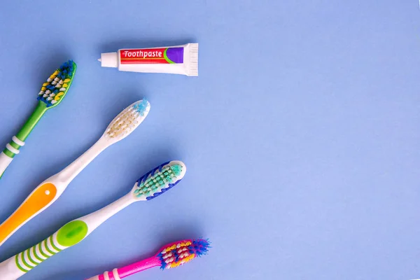 Pasta de dientes pequeña y varios cepillos de dientes desde la vista superior en azul —  Fotos de Stock