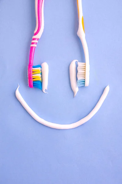 Pasta de dientes pequeña y varios cepillos de dientes como una sonrisa desde la vista superior en azul —  Fotos de Stock