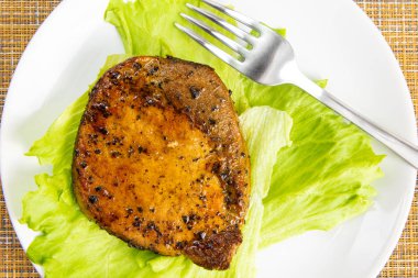 Beyaz bir tabakta marul salata yaprağı ve çatal ile Biftek et