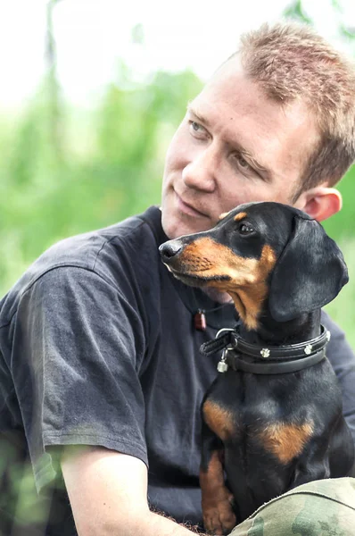 Hombre y perro sentarse en una hierba verde en verano y mirar hacia otro lado —  Fotos de Stock