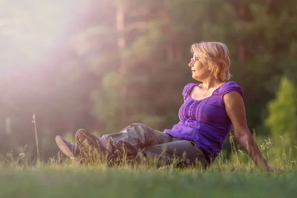 Mujer vista lateral sentada en la hierba y disfrutando del sol en la naturaleza acampando —  Fotos de Stock