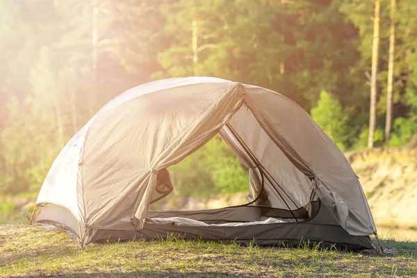 Grått camping tält byggt på grönt gräs nära skog i vild natur med solljus — Stockfoto