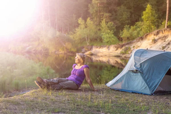 Kvinna sitter i gräset nära camping tält och njuter av sol skenet — Stockfoto
