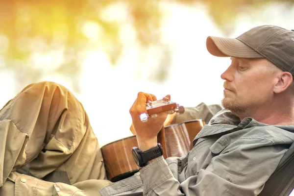 Retrato de un joven con sombrero tocando la guitarra y balanceándose en hamaca de fin de semana por la mañana en el campamento de descanso — Foto de Stock