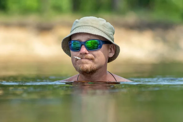 Retrato de un gracioso fumando un cigarrillo, disfrutando nadando en sombrero y gafas de sol. Concepto vacaciones, descanso activo —  Fotos de Stock