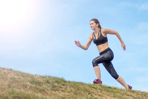 Side view beautiful woman running on the edge of the hill. background blue sky — Stock Photo, Image