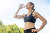Portré fiatal gyönyörű sötét hajú női fitness nő ivóvíz nyári zöld parkban.
