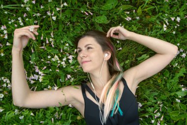 Ön görünüm kadın çimenlerde yatan ve gülümseyen. dinlemek ve kulaklık müzik keyfini çıkarın. yaşam tarzı müzik kavramı.