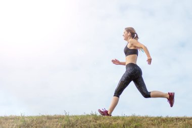 Yan görünüm güzel kadın tepenin kenarında çalışan. arka plan mavi gökyüzü