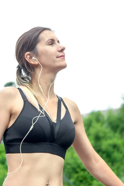 Portrait femme fitness au repos et écoute de la musique sur les écouteurs dans le parc de la ville. Concept de forme physique et style de vie . — Photo