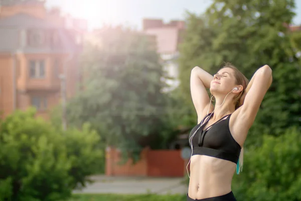 Vue de face femme est étirement et profiter du soleil dans le parc de la ville. Concept de forme physique et style de vie . — Photo