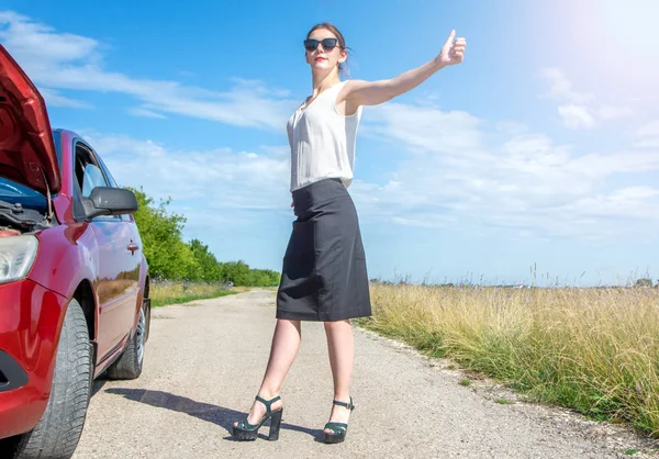 히치하이크 소녀입니다. 도로에 깨진 자동차 근처에 서서 지나가는 차를 잡는 아름다운 비즈니스 소녀. — 스톡 사진