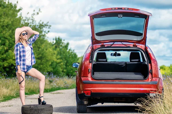Красива дівчина з ключем циліндра змінює колесо в розбитому автомобілі. Заміна шин на стороні дороги . — стокове фото