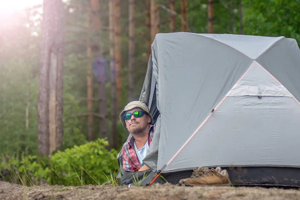 Man i en hatt och solglasögon som ligger i ett tält och röker en cigarett. koncept för resor och Camping — Stockfoto