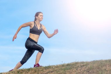 Yan görünüm güzel kadın tepenin kenarında çalışan. arka plan mavi gökyüzü