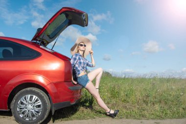 yan görünümü güneş ışığı ile yeşil alan bir arka plan üzerinde arabanın yanında duran büyük bir şapka güzel kız