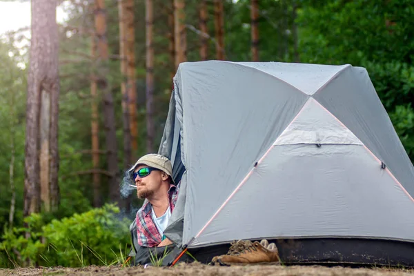 Man i en hatt och solglasögon som ligger i ett tält och röker en cigare — Stockfoto