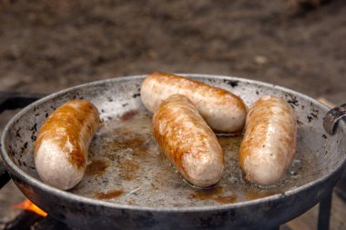 Bir çayır üzerinde duman ve alev ile tavada ızgara sosis. 