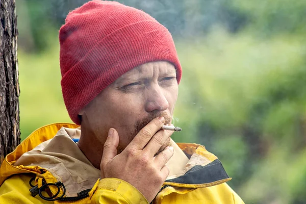 Brutal hombre fumando un cigarrillo en verde bosque, hipster al aire libre —  Fotos de Stock