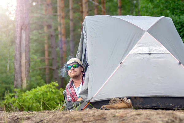 Man i en hatt och solglasögon som ligger i ett tält och röker en cigare — Stockfoto