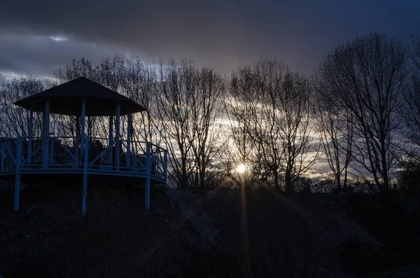 Kahle Äste und Gartenhaus gegen den Sonnenuntergang. dunkler Abend. — Stockfoto