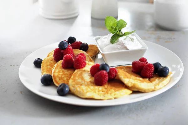 Fluffy pancakes with summer fruits.  A portion of tasty pancakes decorated with berries of raspberries and blueberries, served with yoghurt sauce