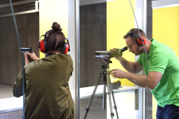 Recreational shooting at the shooting range. The woman shoots from the gun at the shooting range under the supervision of an instructor.