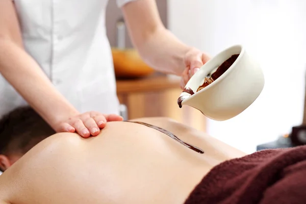 Chocolate back massage. A man on a massage treatment in a wellness salon.