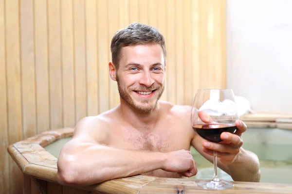 A bath in wine, a man relaxes in the spa with a glass of red wine.