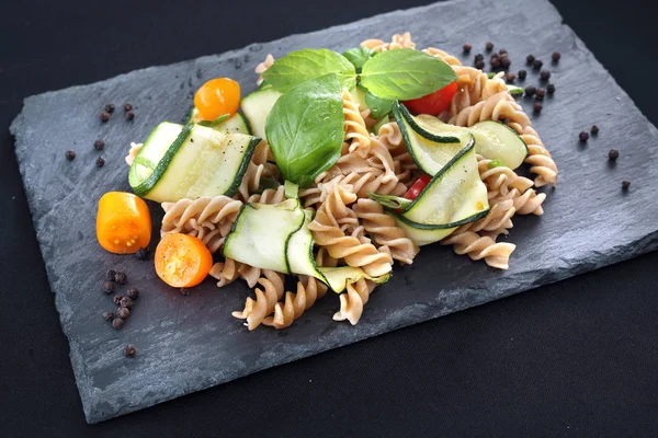 Spiral pasta with vegetables. Pasta salad with zucchini and tomatoes served on a black plate. — Stock Photo, Image