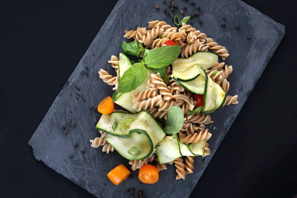 Pasta salad with zucchini and tomatoes served on a black plate. — Stock Photo, Image