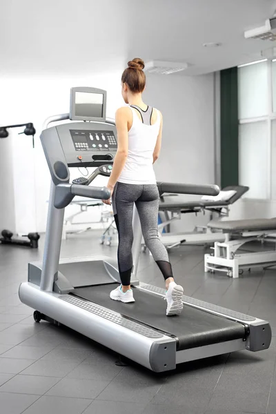 Genç bir kadın bir egzersiz odasında otomatik bir koşu bandı üzerinde çalışan. — Stok fotoğraf
