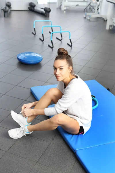 A young, attractive woman in an exercise room on a blue sports mattress. — Stock Photo, Image