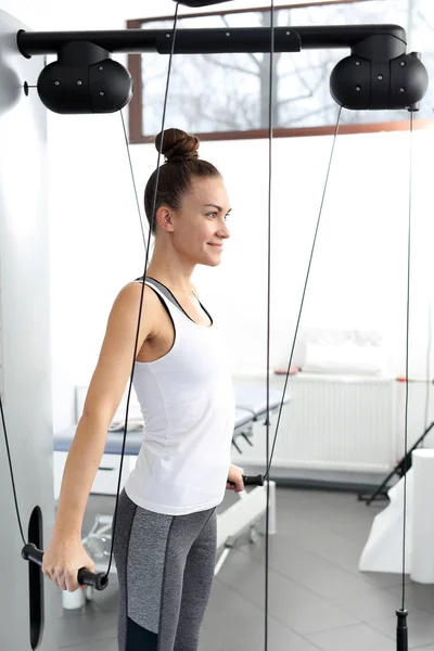 Rehabilitación y ejercicios de una joven en una máquina de entrenamiento con una carga . —  Fotos de Stock