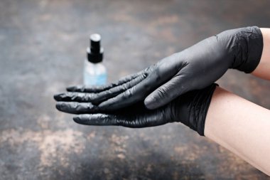 Siyah koruyucu eldivenli eller antivirüs sıvısıyla dezenfekte edilmiş. Kadın, alkol bazlı antibakteriyel sıvıyla uygun el dezenfeksiyonu aşamalarını gösteriyor. El dezenfeksiyonu ve hijyen.