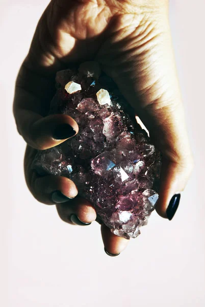 Hand holding gemstone Amethyst closeup with rock Quartz crystals.